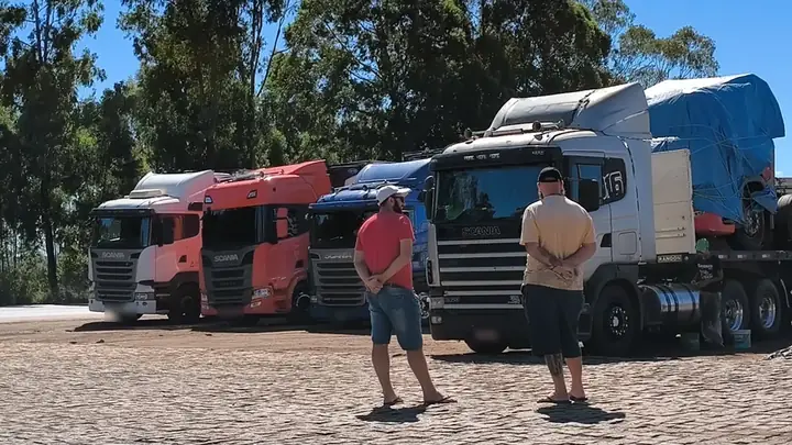 Dois motoristas no pátio em frente a uma fila de caminhões Scania