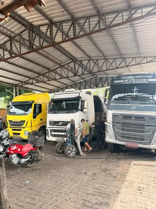 Iveco amarelo, Volvo branco e Volvo Globetrotter em manutenção no pátio coberto